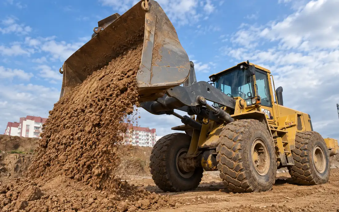 Wheel loader discharging a bucket of soil on a site being prepared
