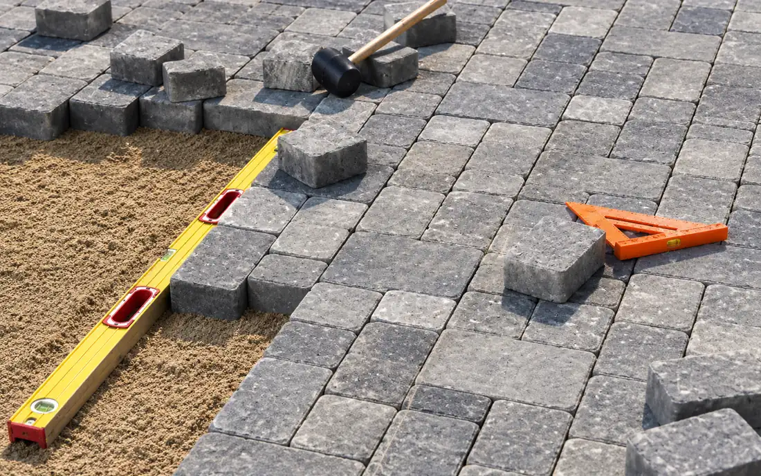 Interlocking pavers being laid on a sand bed with a spirit level and rubber mallet
