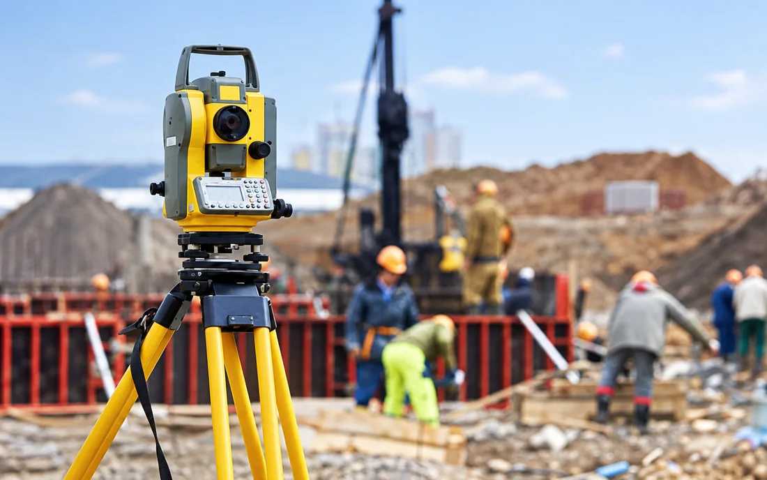 Total station on a tripod in front of foundation works in progress