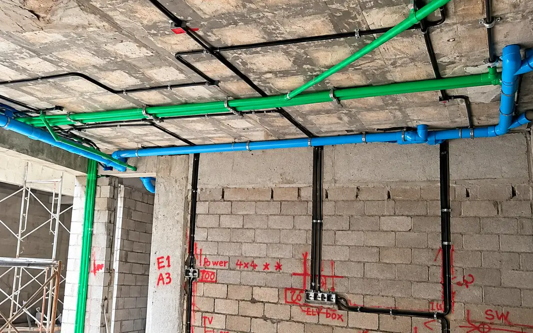 Colour-coded water pipework and electrical conduit on the ceiling of a building under construction